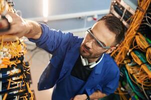 In, blue colored uniform. Young man is working with internet equipment and wires in server room photo