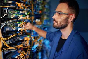 Repairman, is busy and working with internet equipment and wires in server room photo