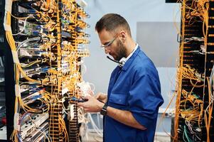 In blue colored, uniform. Young man is working with internet equipment and wires in server room photo