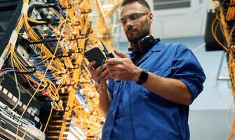 View, from below. Young man is working with internet equipment and wires in server room photo