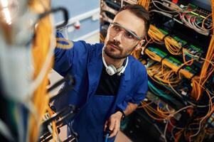 Looking, up, management of cables. Young man is working with internet equipment and wires in server room photo