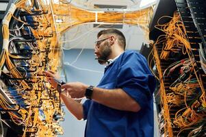 Professional ,device in hands. Young man is working with internet equipment and wires in server room photo
