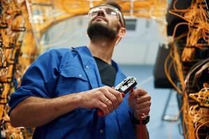Busy by, cutting the, wire. Young man is working with internet equipment in server room photo