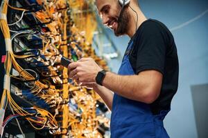 Administrator, is busy. Young man is working with internet equipment and wires in server room photo