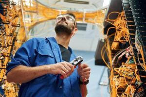 Busy, by cutting the wire. Young man is working with internet equipment in server room photo