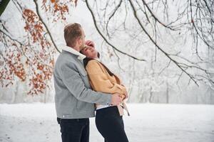 Standing, and enjoying snow. Beautiful couple are together on the field of forest photo