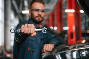 Showing ,tool ,that is in the hand. Car repairman is in the garage with automobile photo
