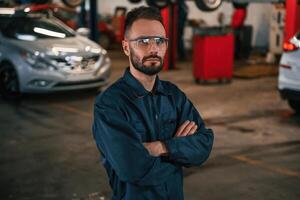 Standing and posing,. Car repairman is in the garage with automobile photo