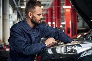 Busy,, car repairman is in the garage with automobile, fixing it photo