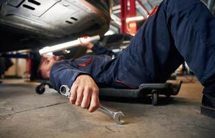 Lying, down on the ground. Car repairman is in the garage with automobile photo
