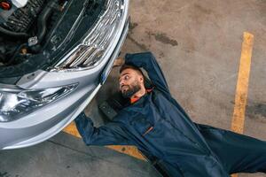 On the, ground with tool. Car repairman is in the garage with automobile photo