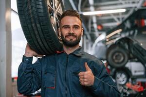 With, brand new tire. Car repairman is in the garage with automobile photo