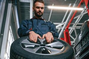 With ,,brand new tire. Car repairman is in the garage with automobile photo