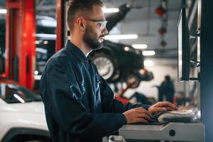 Working ,,by computer. Car repairman is in the garage with automobile photo