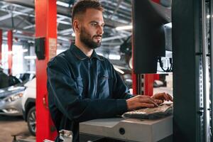 Working by computer.. Car repairman is in the garage with automobile photo
