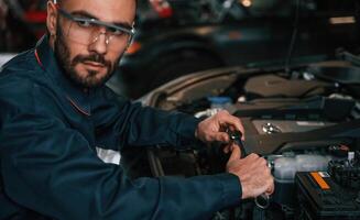 Hood is ,,opened, fixing. Car repairman is in the garage with automobile photo