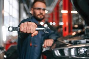 Showing ,tool that is in the hand. Car repairman is in the garage with automobile photo