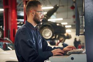 Working, by computer. Car repairman is in the garage with automobile photo
