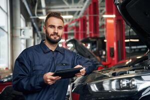 Using ,tablet. Car repairman is in the garage with automobile photo
