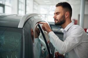 Looking, at polished surface. Worker in formal clothes is in the auto salon photo