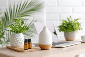 Aromatherapy diffuser with essential oils, plants, and laptop on a wooden table in a bright, modern workspace, wellness and relaxation concept photo