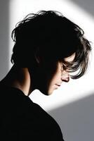 Young man with messy hair looking down in a studio with hard lighting creating shadows on face and background photo