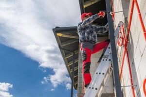 Worker Climbs Ladder to Install Gutter on Construction Site photo