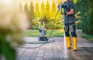 Man Using Pressure Washer to Clean Patio in Sunny Garden Setting photo