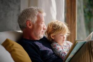 Grandfather reading a book to grandchild on sofa at home photo