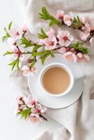 Cup of coffee with milk surrounded by peach tree flowers on white background photo