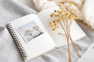 Open notebook with photo and dried flowers resting on soft blanket