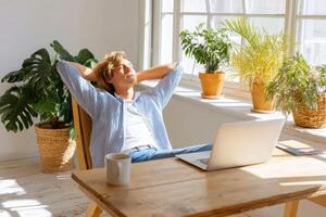 Remote worker enjoying a mid-day break in a bright home office surrounded by plants, relaxing with a laptop, and embracing a peaceful atmosphere, wellness concept photo