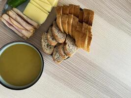 Selection of fresh bread, cheese, and cold cuts with a bowl of soup on a wooden table photo