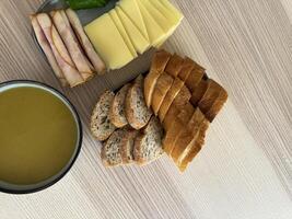 Light meal featuring bread, cheese, ham, and soup on a wooden table photo
