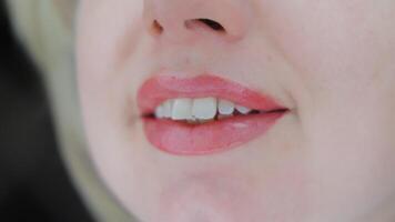 Close-up of woman lips with soft pink permanent makeup, showing natural shape, gloss, and smooth skin texture in daylight studio environment with delicate smile video