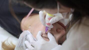 Close-up of cosmetologist performing permanent eyelash line tattoo, precise pigment application between lashes using tattoo device during cosmetic procedure video