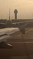 Airport at sunset, view from an airplane window, planes and terminals in the distance . Vertical video