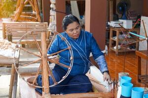 Asian woman, a member of a community hand weaving group, spins thread with A spinning machine which is a tool used to spin cotton into tight threads threads photo