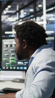 Vertical Data center engineer in wheelchair and colleague oversee automated tasks using node tree programming tool. Inclusive server farm team adjusts system settings based on AI analytics, camera A video