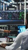 Vertical Manager supervising data center engineer using AI neural network models to configure hardware. Team leader overseeing employee using machine learning programming language to optimize systems, camera A video