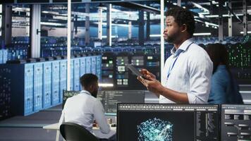 Data center engineer using tablet to interpret data analytics graphs. Server room worker using artificial intelligence displaying system performance predictive metrics, camera A video