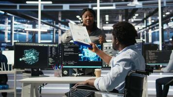 Server hub admin with paraplegia receiving paperwork documents from colleague, using AI node tree software. Man with disability in data center getting documentation files from coworker, camera A video