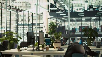 Modern office workspace desk with computer monitors displaying graphs, charts and data analytics, surrounded by plants and paperwork with city environment background, panning shot video