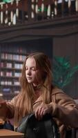 Vertical Female college student reads and writes detailed notes for a new course, studying political science for upcoming lecture in a library setting at university. Girl consults database. Camera B. video