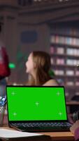Vertical Young student working with a green screen in the university campus library, collecting academic information from verified educational sources. Pupil using research tools. Camera A. video