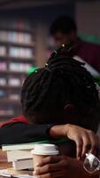 Vertical African american student falling asleep on books pile in the campus library, dealing with burnout and struggling to graduate college. Young pupil with fatigue tries to study at night. Camera A. video