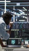 Vertical Data center engineering team uses artificial intelligence deep learning models to configure gear. Teamworking colleagues work on AI programming language in server farm, optimizing system, camera A video