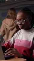 Vertical Young black learner focusing on literature assignment by gathering data from the database at the university library, using research tools to gather more academic information. Camera B. video