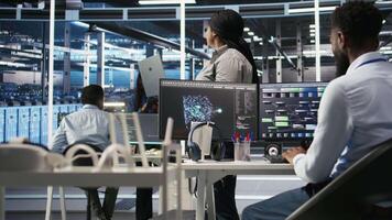 Data center admin using laptop to do node tree programming, optimizing resource allocation. Woman in server room uses predictive AI visualization systems on notebook for maintenance planning, camera A video
