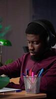 Vertical African american guy student uses ambient focus music to help with school assignment, collecting citations from books and other academic sources from the university database. Camera A. video